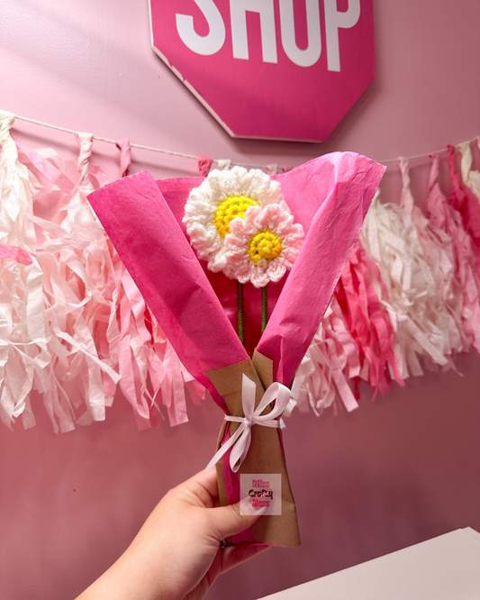 Small Bouquet of flowers wrapped in pink paper with a decorative bow, held against a pink background with 'SHOP' sign.