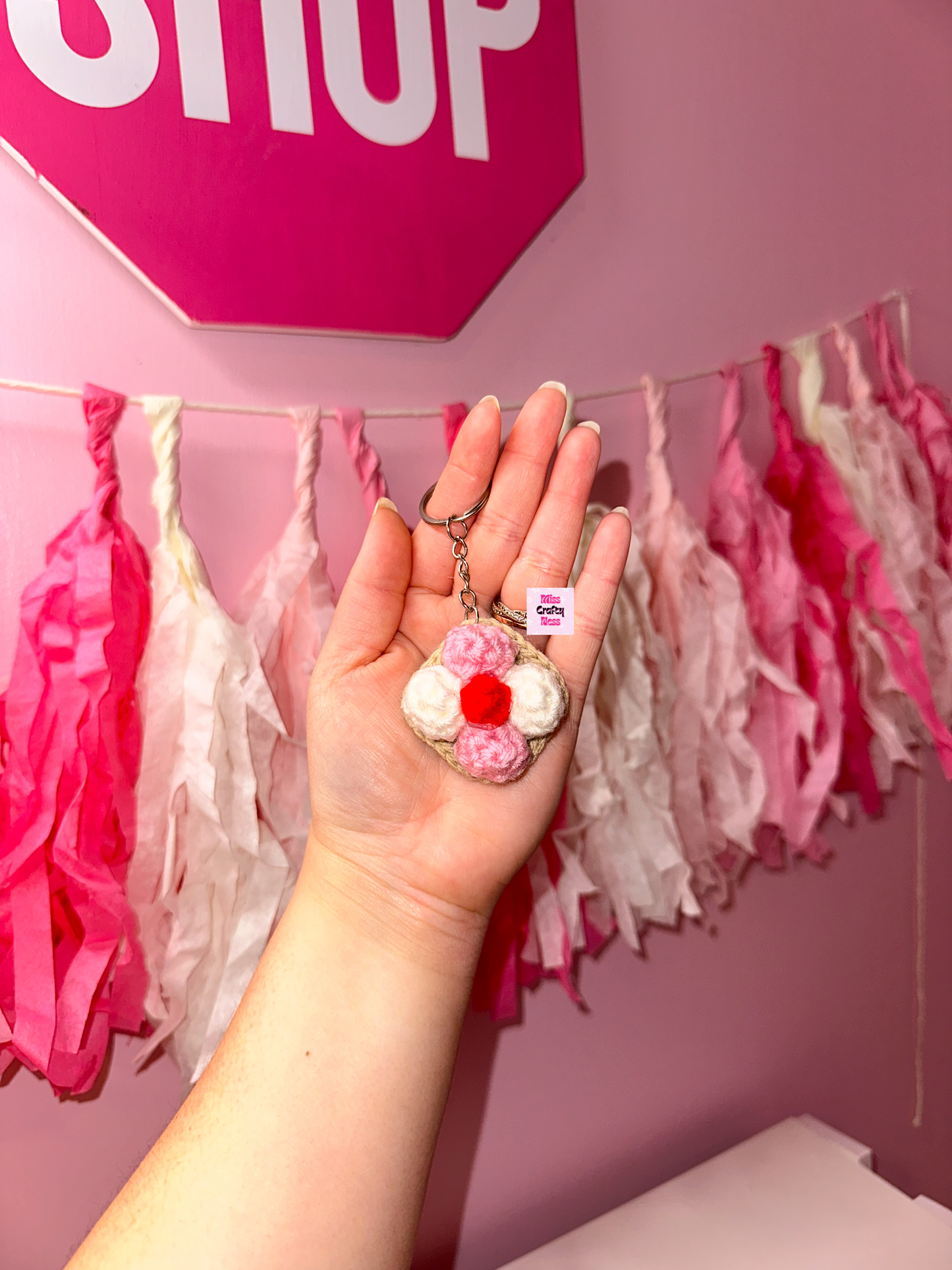 Hand holding a crochet coconut cookie keychain in front of a pink wall with tassels.