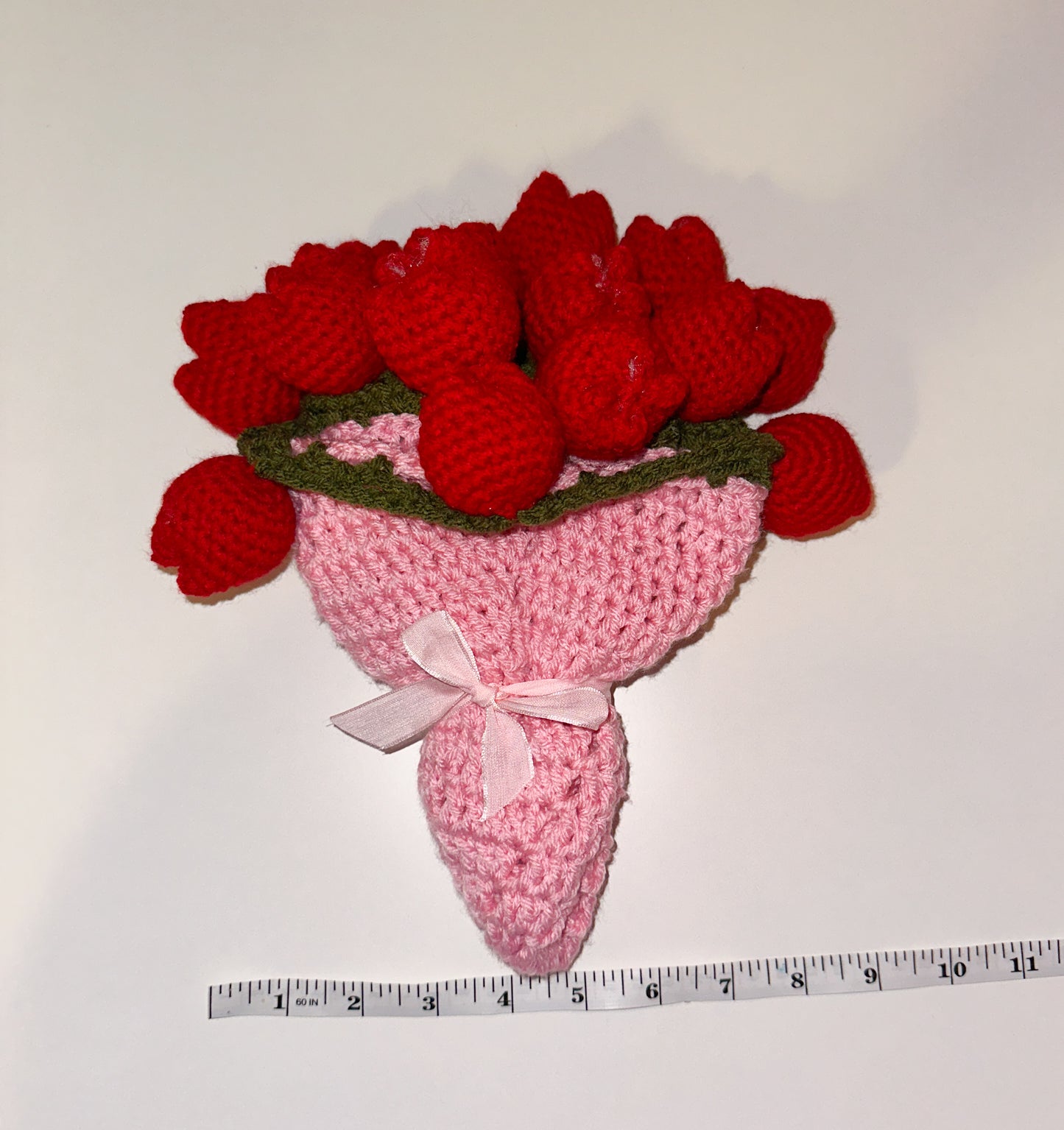 Crocheted bouquet of red flower tulips with a pink base above a measuring tape with a white background