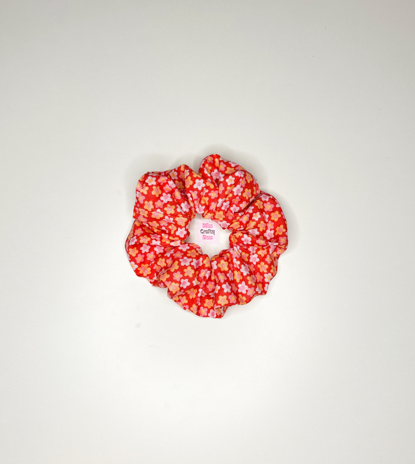 A red with pink flowers handmade scrunchie made from cotton fabric, displayed on a white background.
