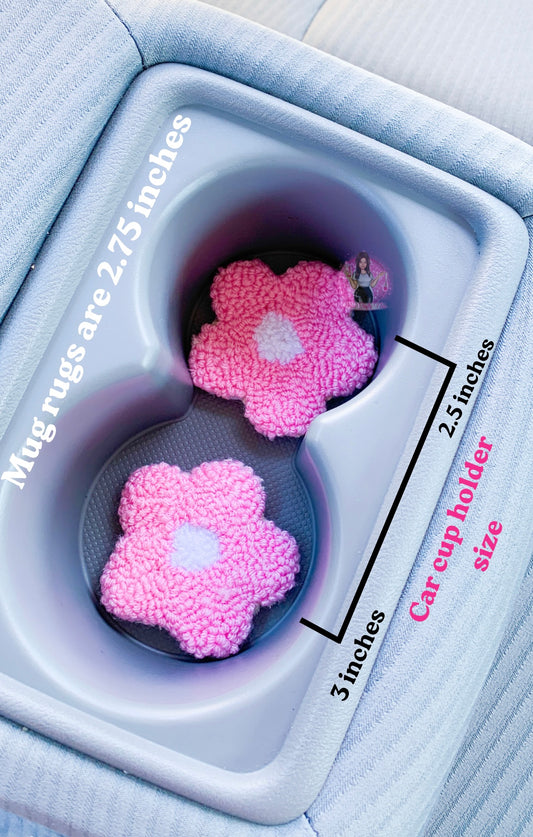 Two pink flower shaped car coasters placed in a vehicle cup holder with words reading ‘Mug rugs are 2.75 inches’ and ‘car cup holder size’ with ‘3 inches’ and ‘2.5 inches’ pointing to cup holders.