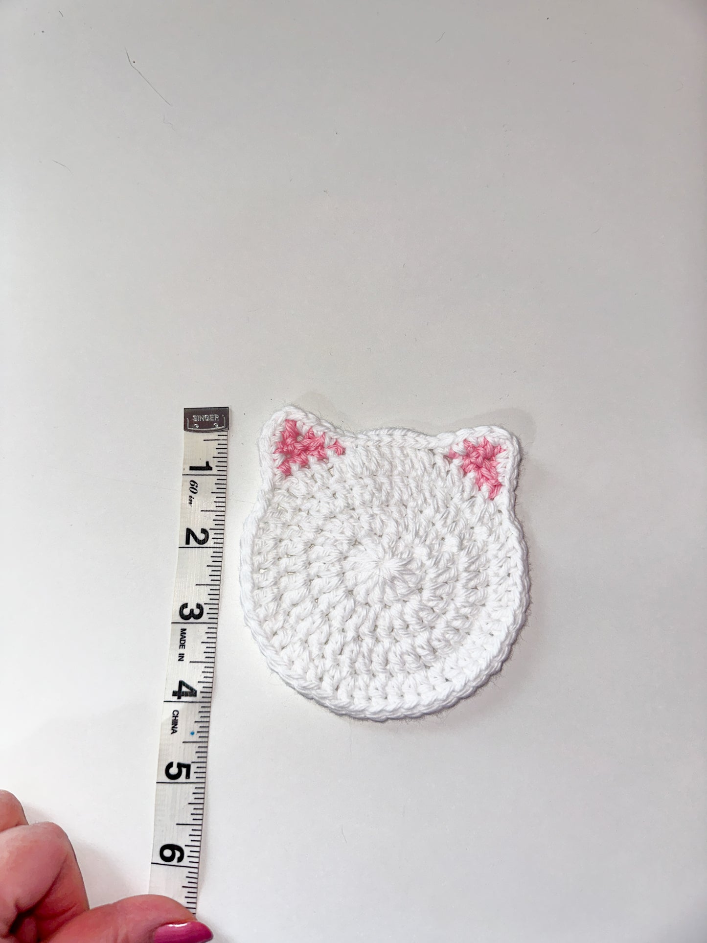 White crochet cat-shaped coaster next to a ruler on a white background