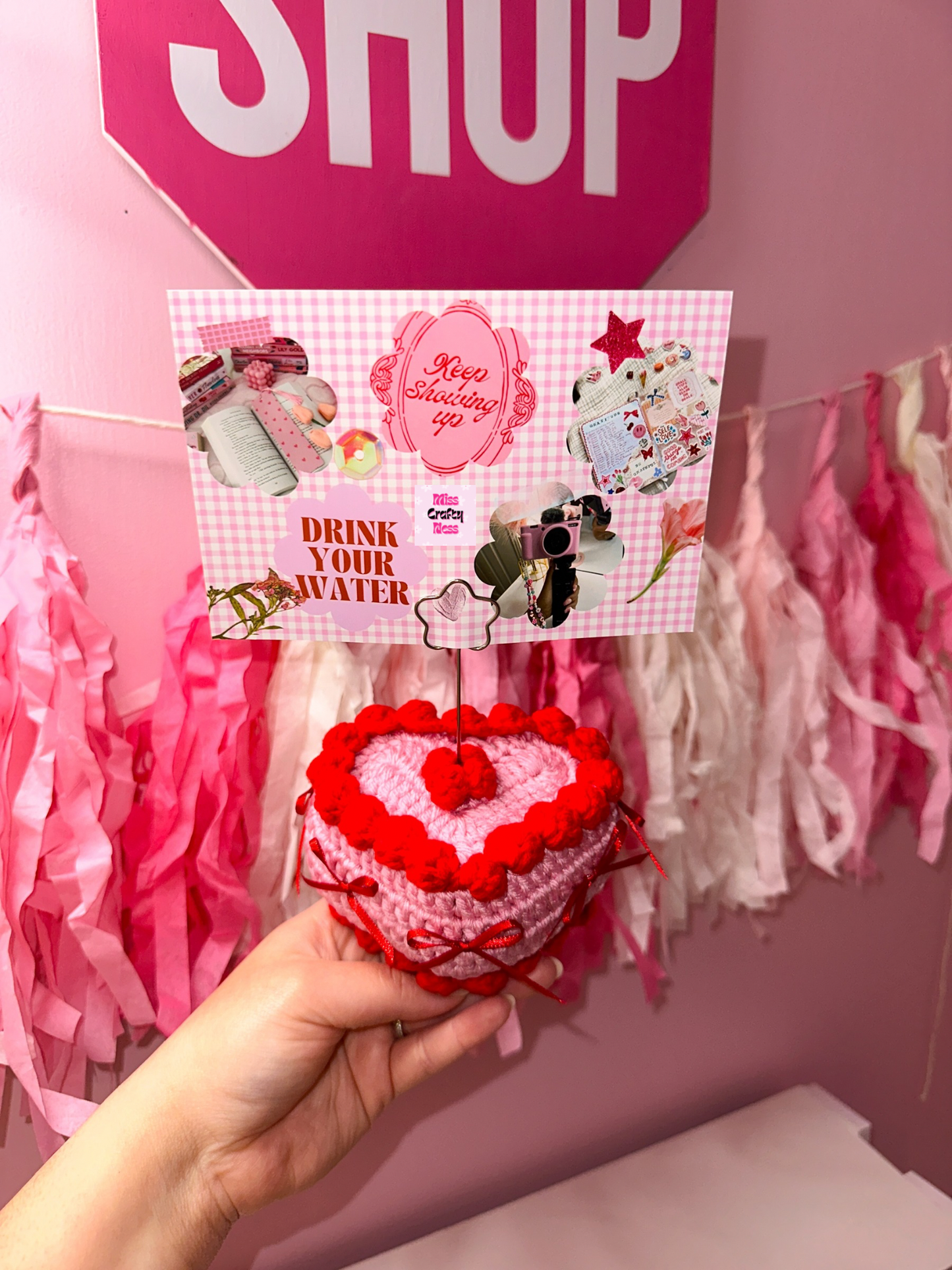 Pink Heart-shaped crocheted cake holding a photo of a vision board against a pink background