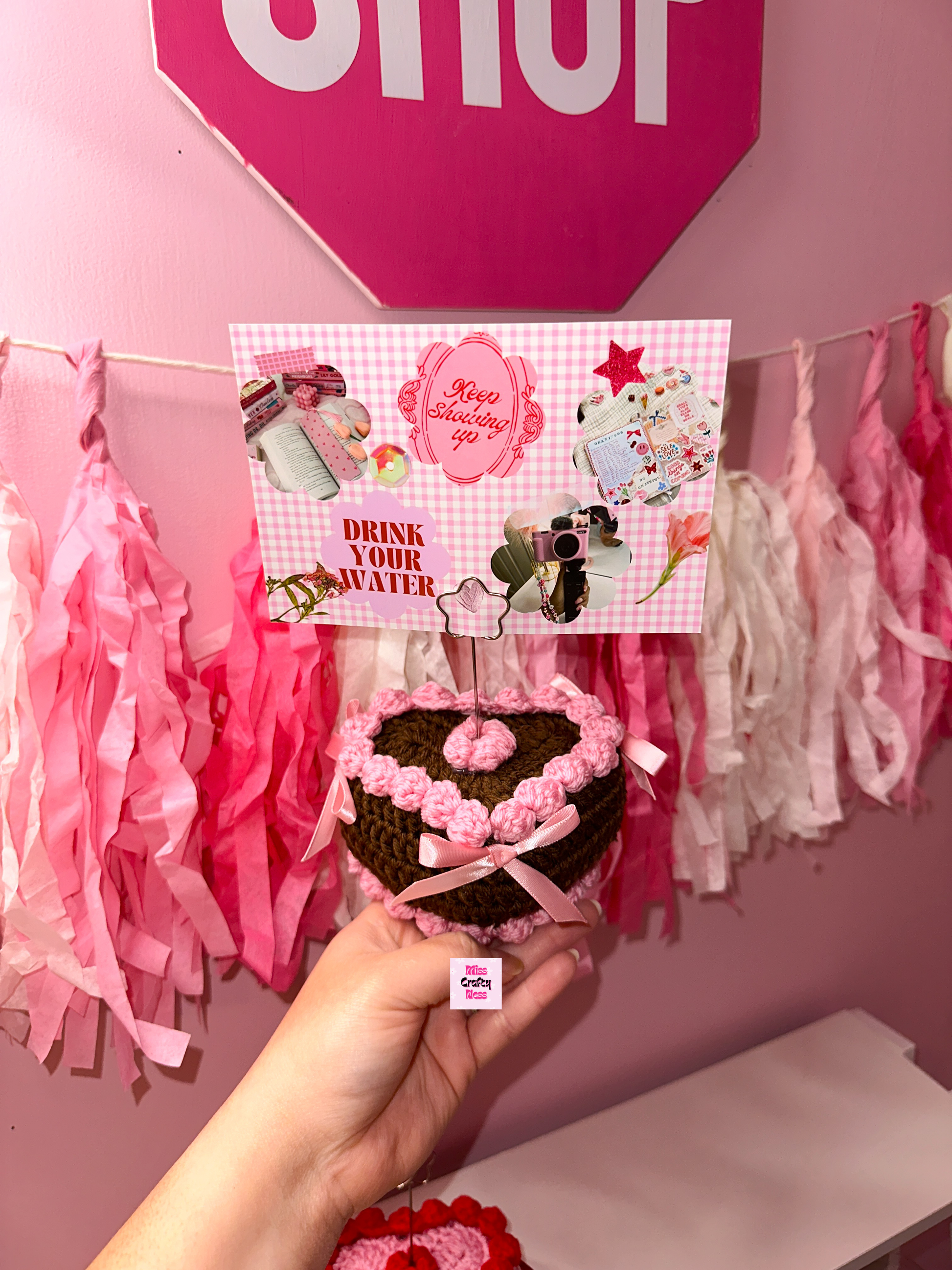 Hand holding a crochet cake with a photo on the top, with a pink decorated background.