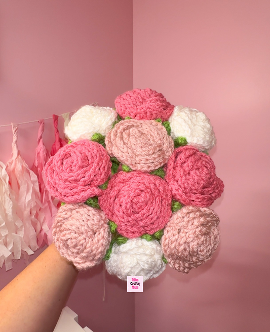 Crocheted rose flower bouquet with pink, white, and green colors against a pink background.