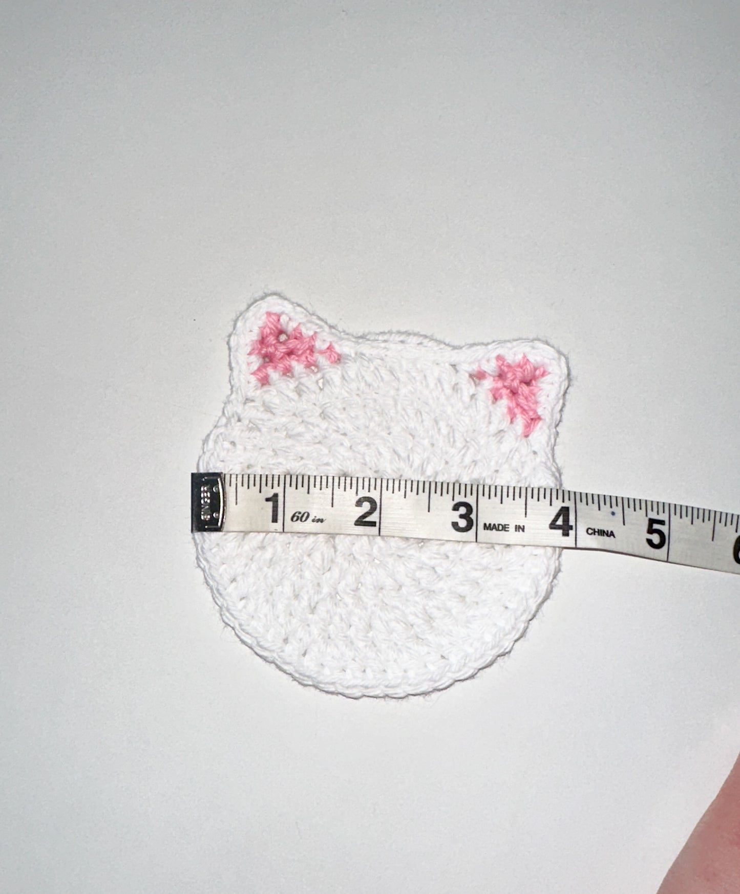 White crochet cat-shaped coaster on a white background, measured by a tape measure.