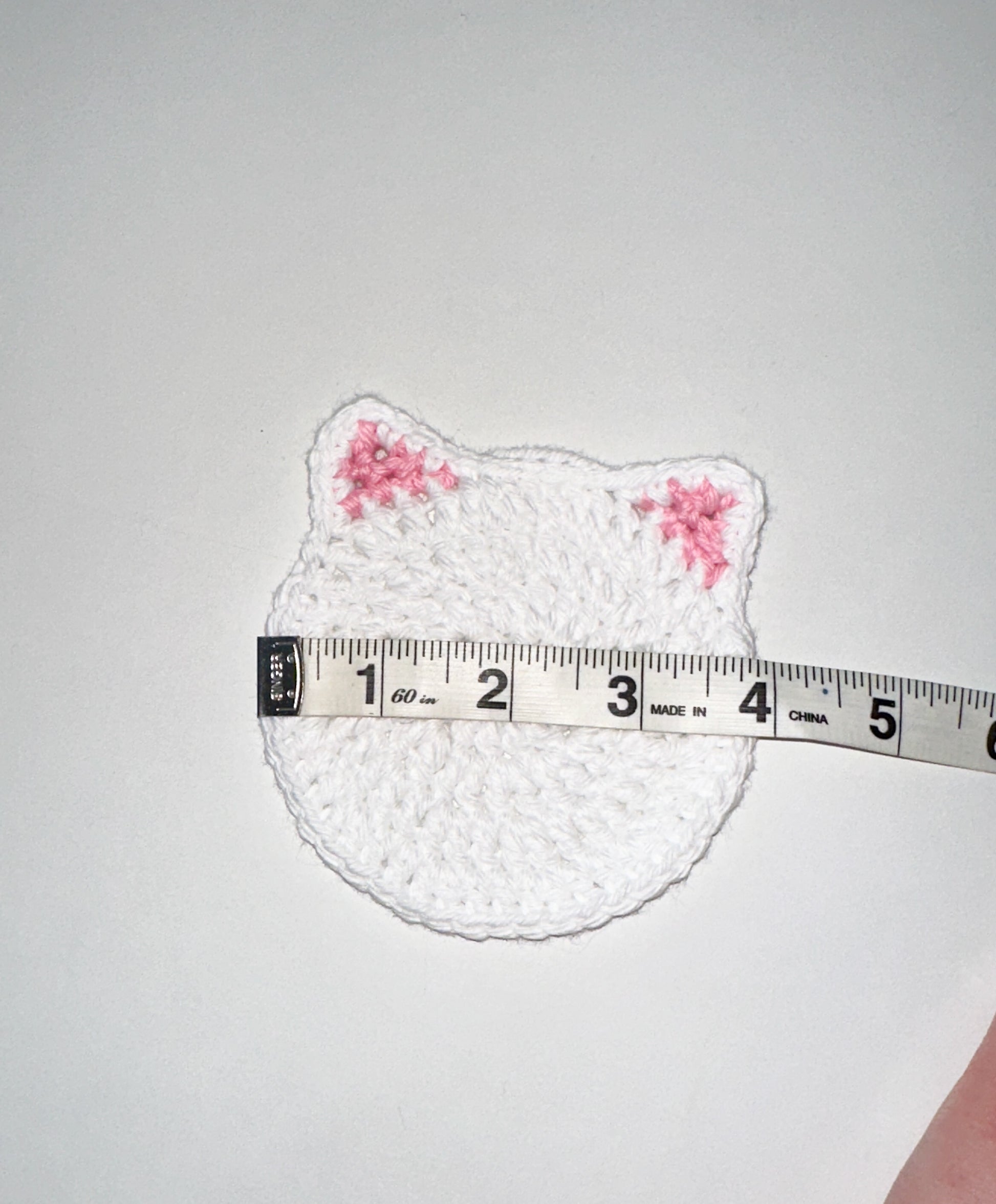 White crochet cat-shaped coaster on a white background, measured by a tape measure.