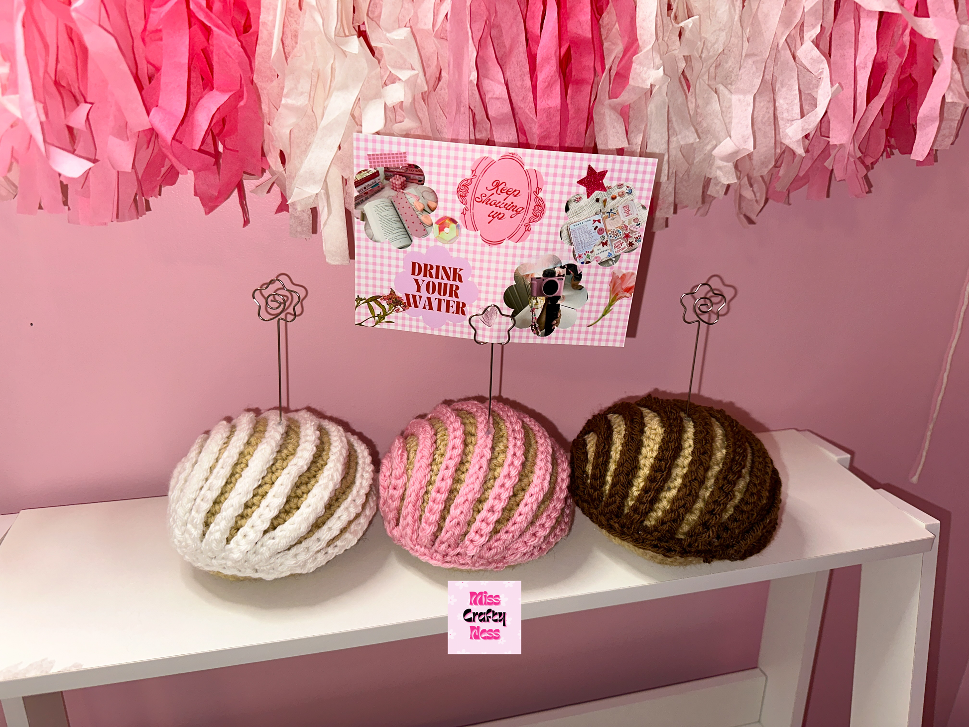 Crochet sweet bread photo holder item on a white table with pink and white tassels in the background.