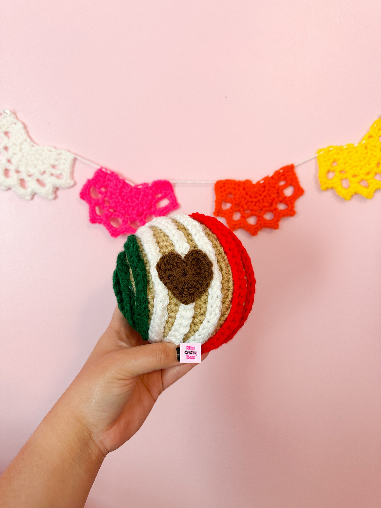 Hand holding a crocheted sweet bread with a heart-shaped object with colorful doilies in the background