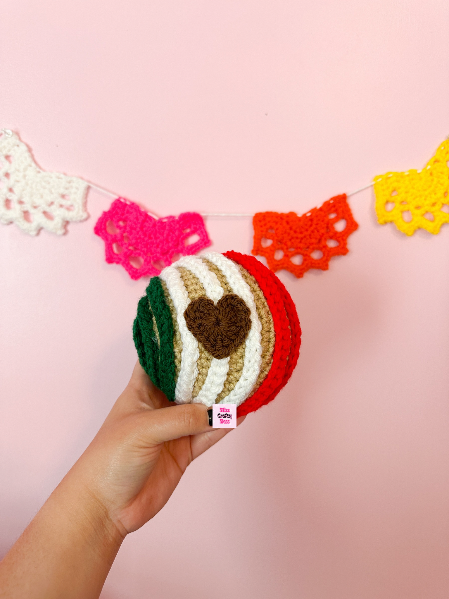 Hand holding a crocheted sweet bread with a heart-shaped object with colorful doilies in the background