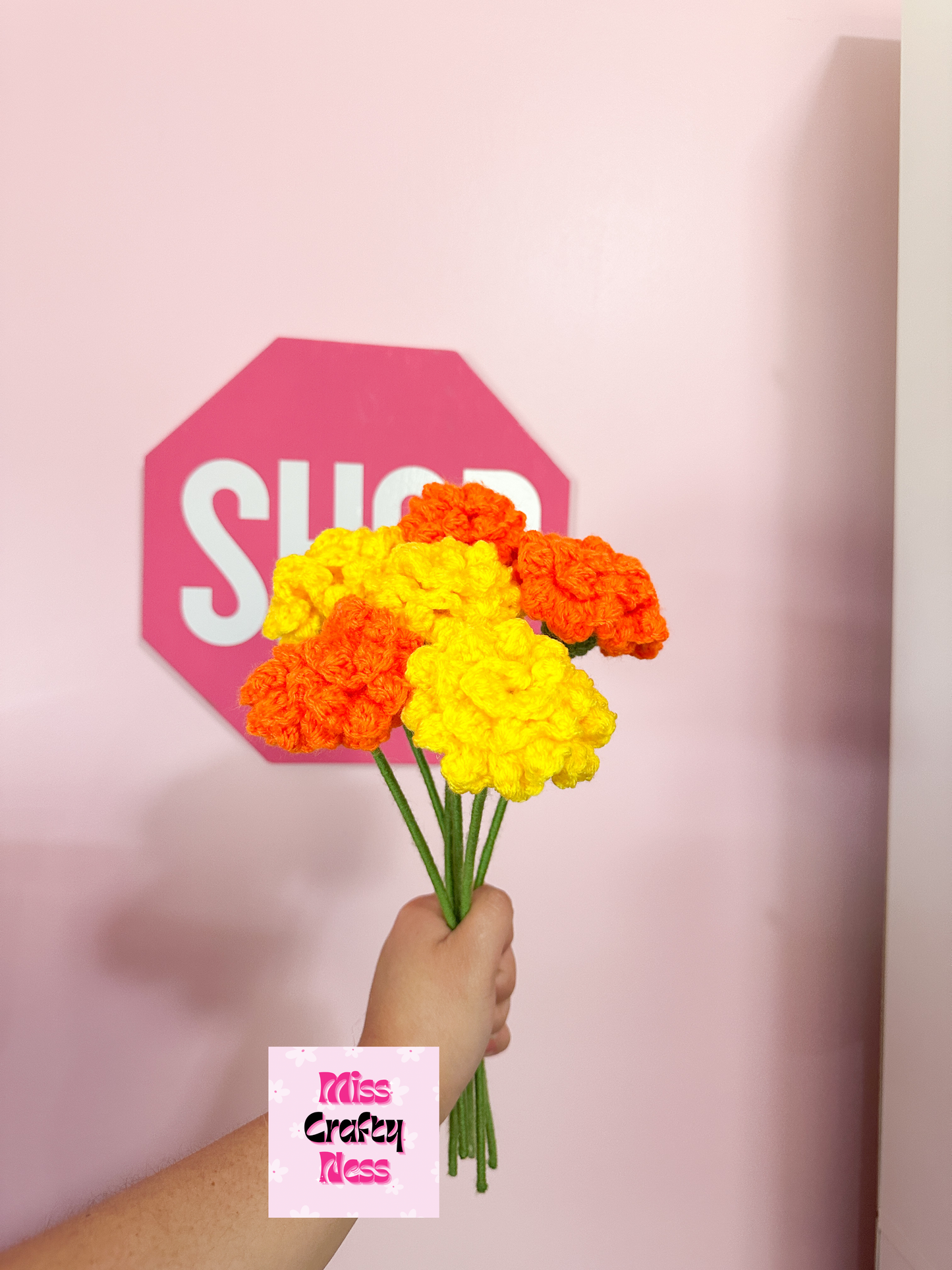 Hand holding a bouquet of yellow and orange flowers in front of a pink sign. 