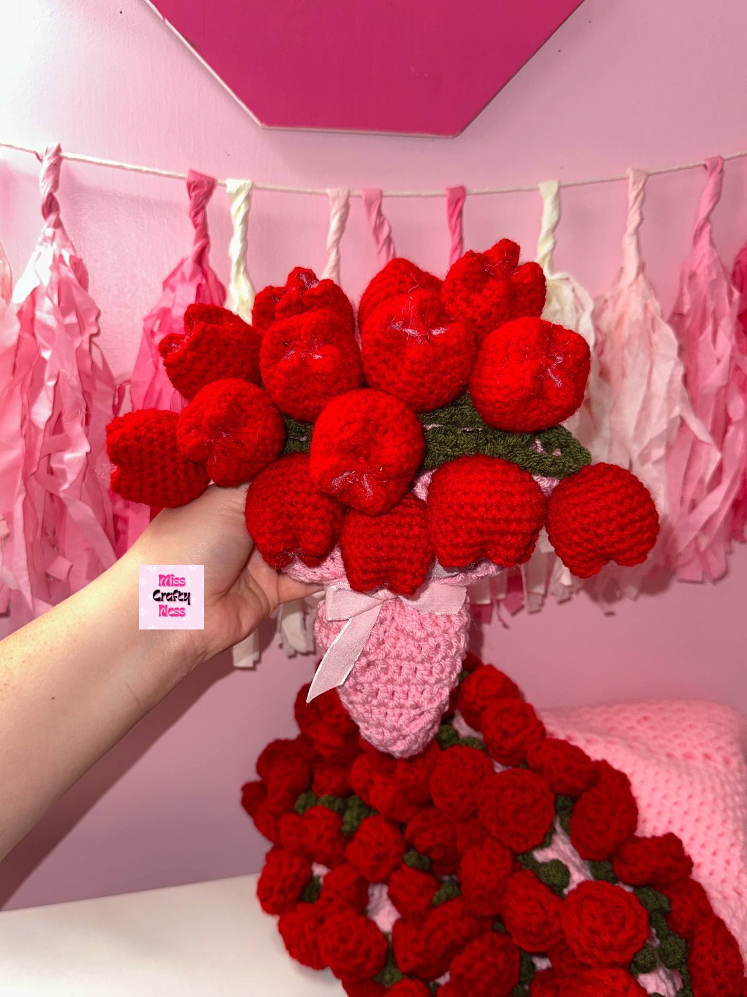 Bouquet of red crocheted tulips with a pink base held against a pink background with decorative ribbons.