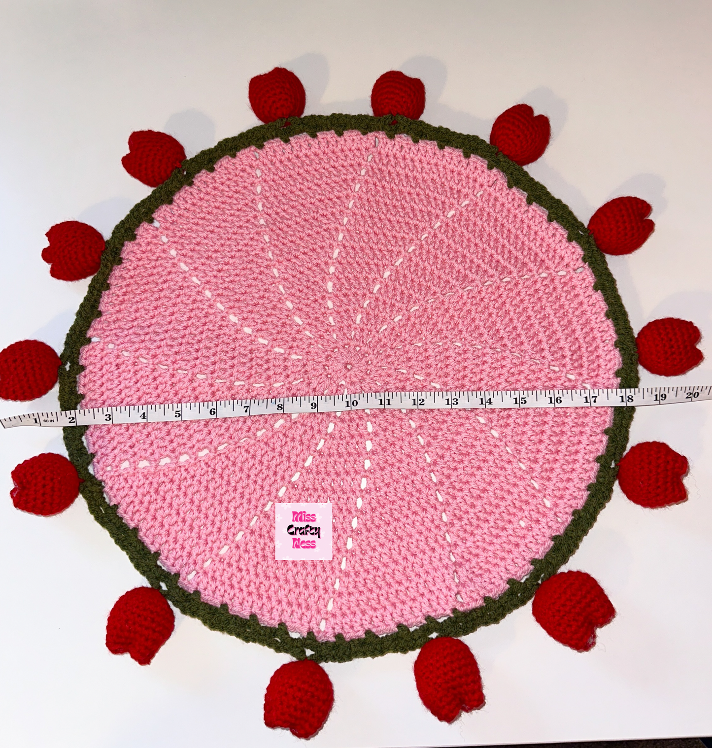Pink crocheted round blanket with red tulip bulbs and a measuring tape on a white background