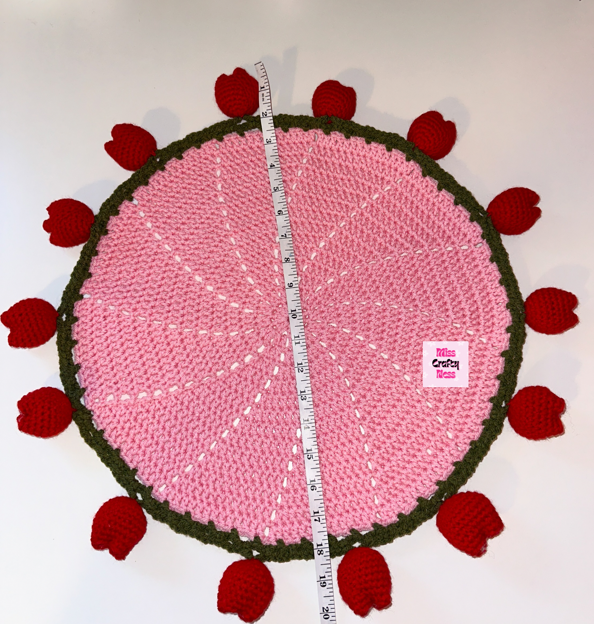 Pink crocheted round blanket with red tulip bulbs and a measuring tape on a white background