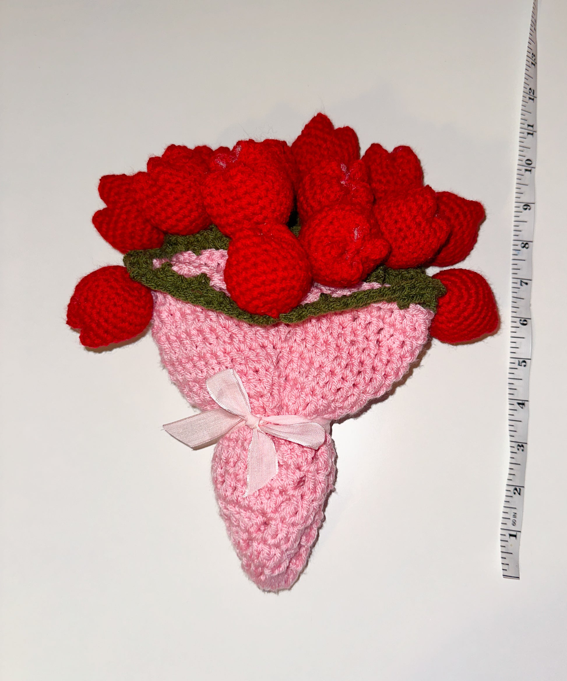 Crocheted bouquet of red flower tulips with a pink base next to a measuring tape with a white background 