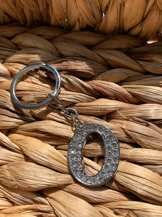 A bling letter keychain with a crystal-encrusted letter 'o’ on a woven background.