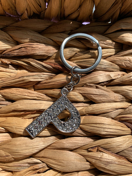 A bling letter keychain with a crystal-encrusted letter 'p’ on a woven background.